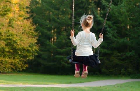 a little girl sitting on a swing in a park